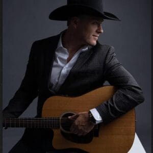 A man in a hat plays an acoustic guitar in moody lighting.