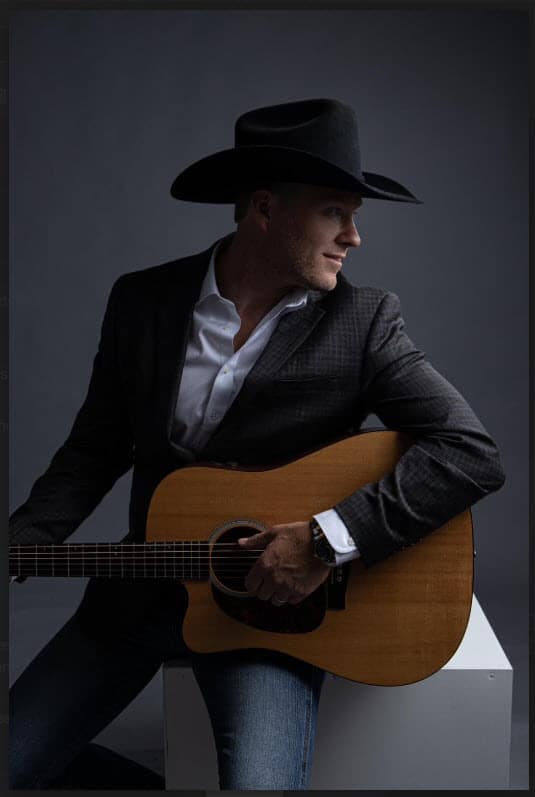 A man in a hat plays an acoustic guitar in moody lighting.