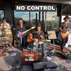 Band performing outdoors beneath "NO CONTROL" sign