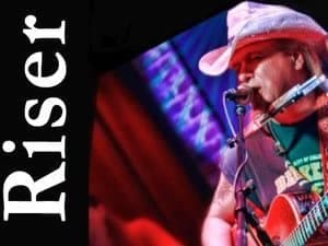 Musician playing harmonica on stage with colorful background lighting.